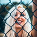 Blonde woman behind a chainlink fence